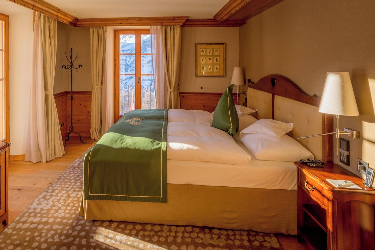A hotel room with a bed, a desk with a television, a coat rack, and a window with curtains.