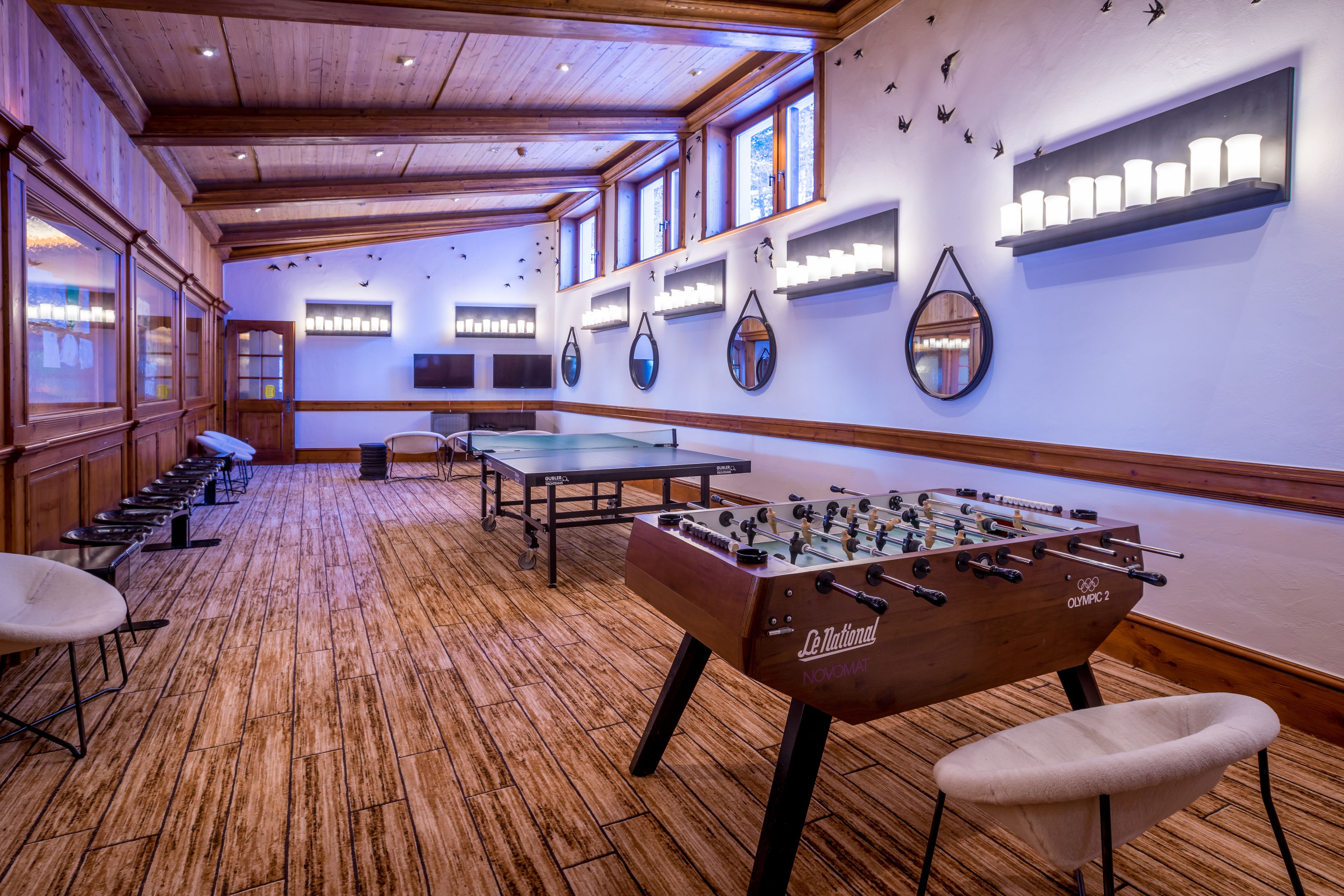 A room with wooden flooring, a foosball table, and several tables and chairs.