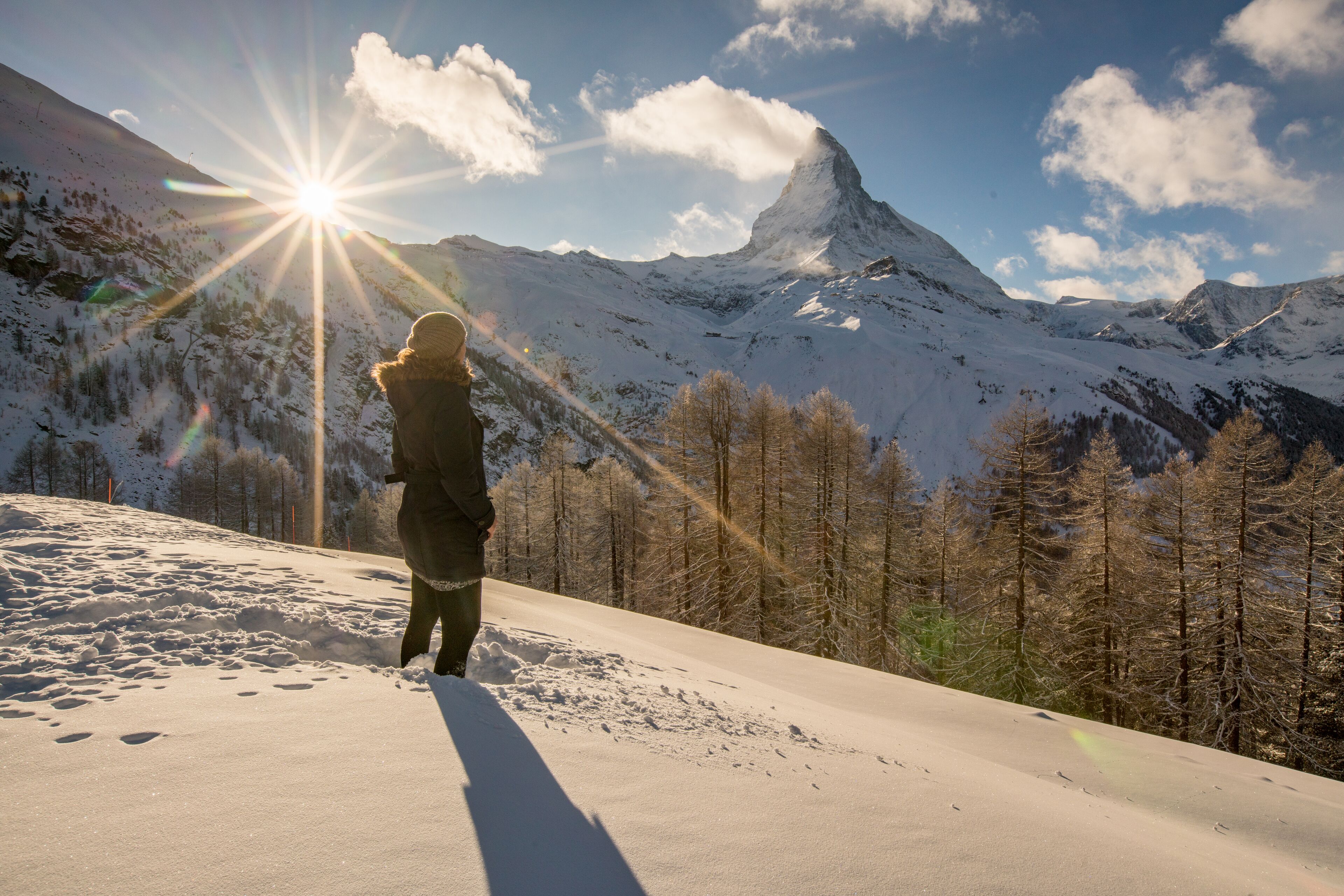 A person standing on a snow-covered slope with a mountain in the background.