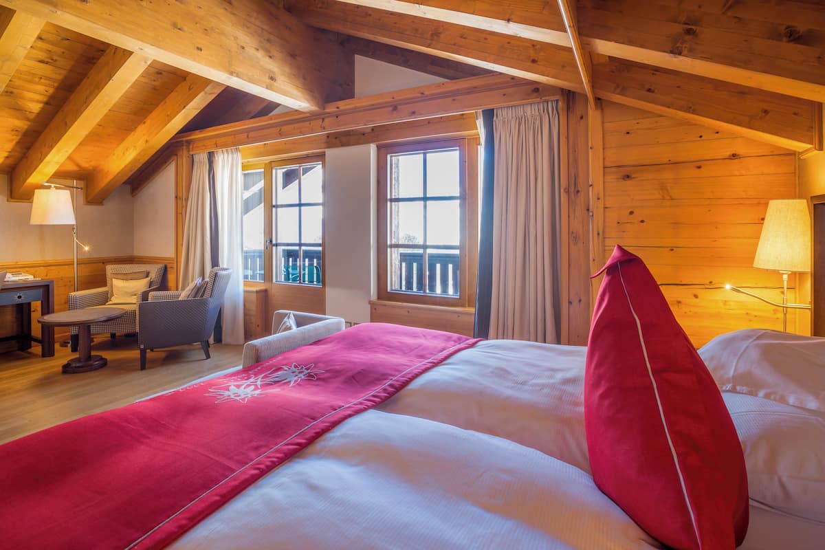 A cozy room with a bed, a chair, a table, and a window with curtains.