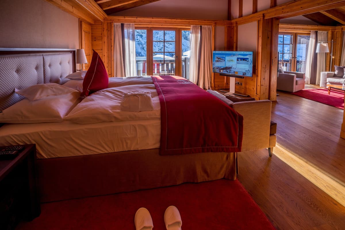 A hotel room with a large bed, a TV, wooden walls, and a view of the outdoors.