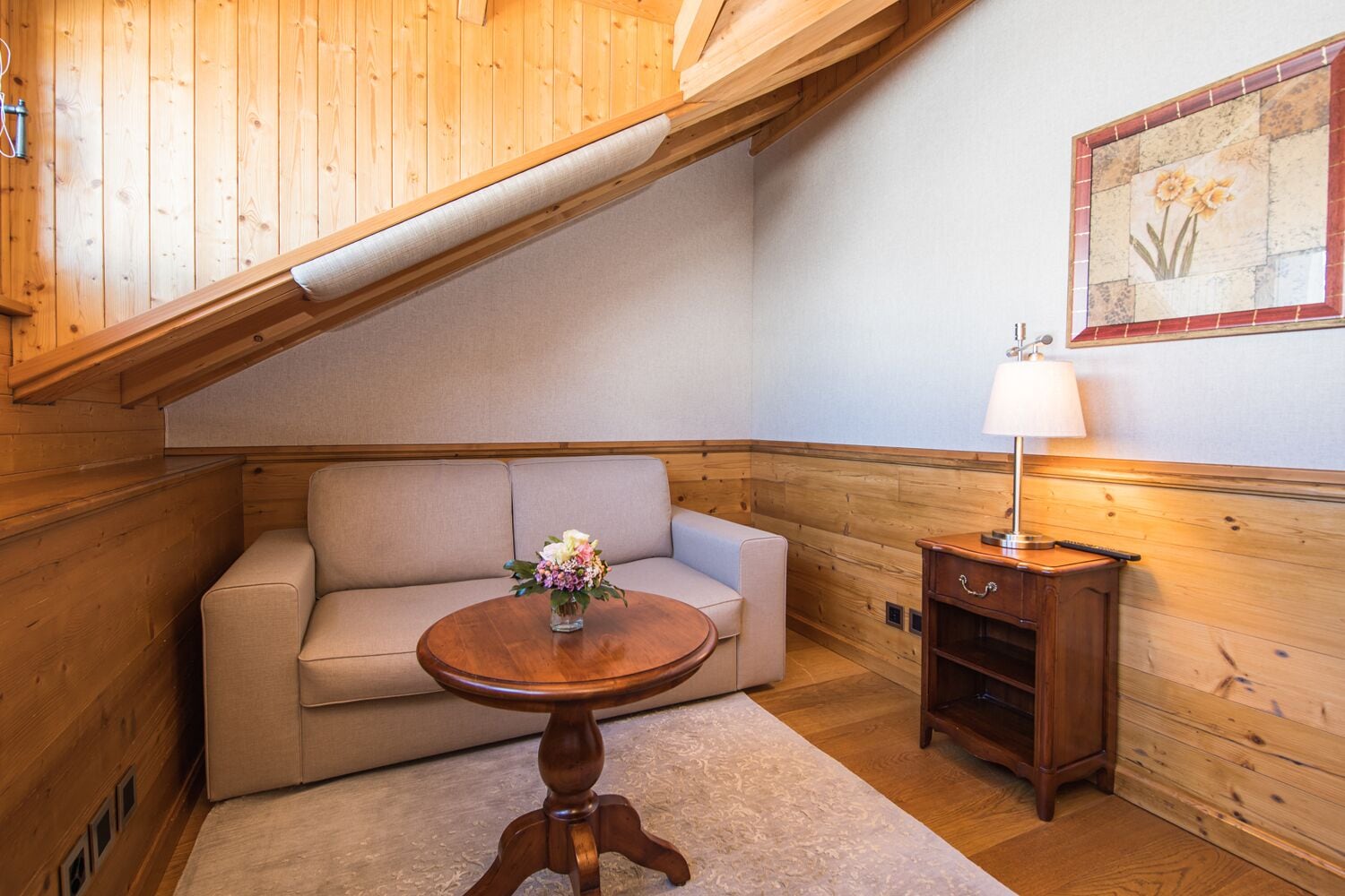 Un coin douillet avec un canapé, une table en bois ornée d’un vase de fleurs, une lampe et un meuble en bois.
