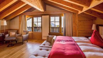 Una camera accogliente con soffitto in legno, un letto grande con lenzuola rosse, una poltrona e un tavolino.