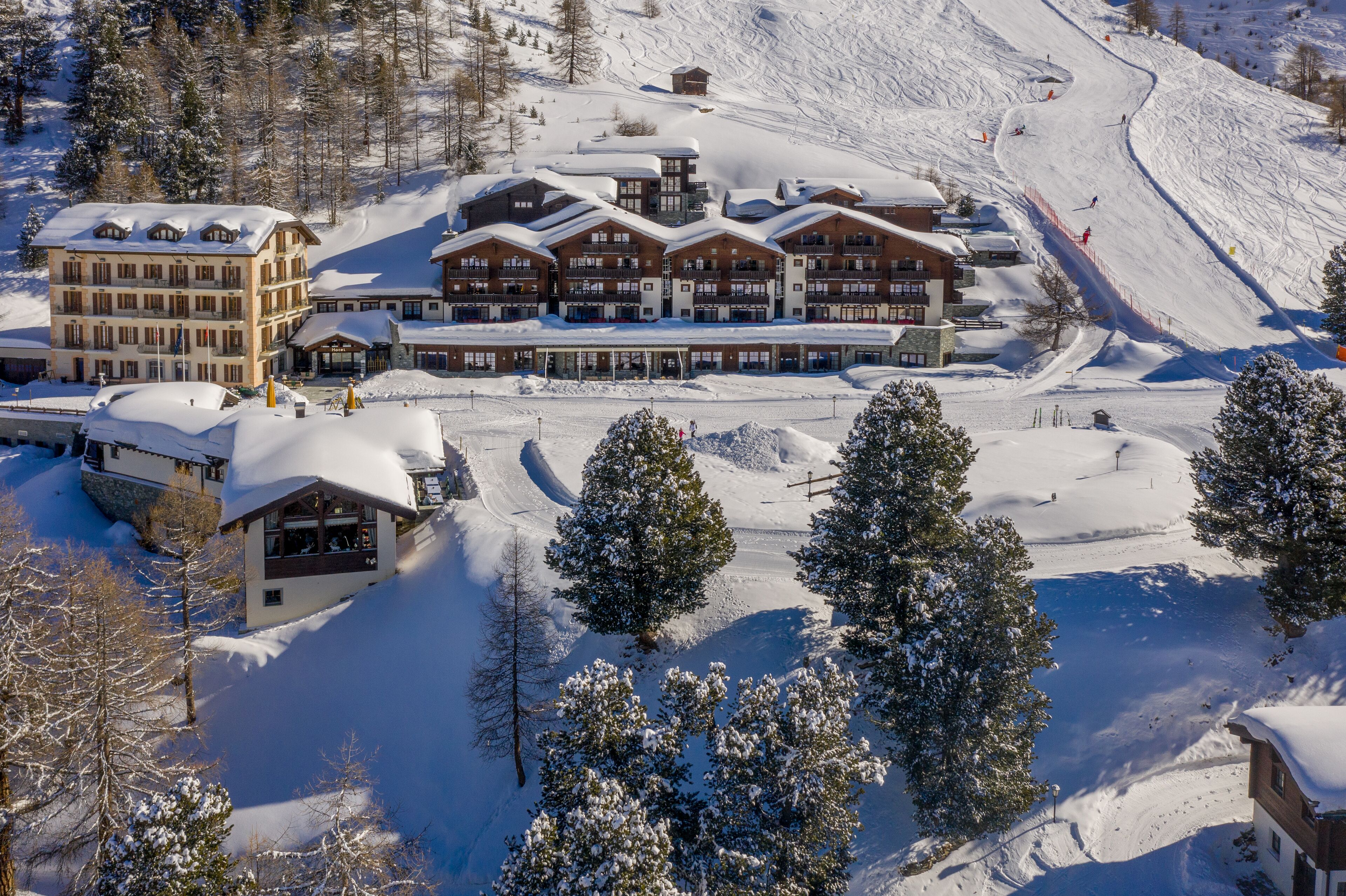 Un chalet enneigé comprenant plusieurs bâtiments, des pistes de ski et des arbres.
