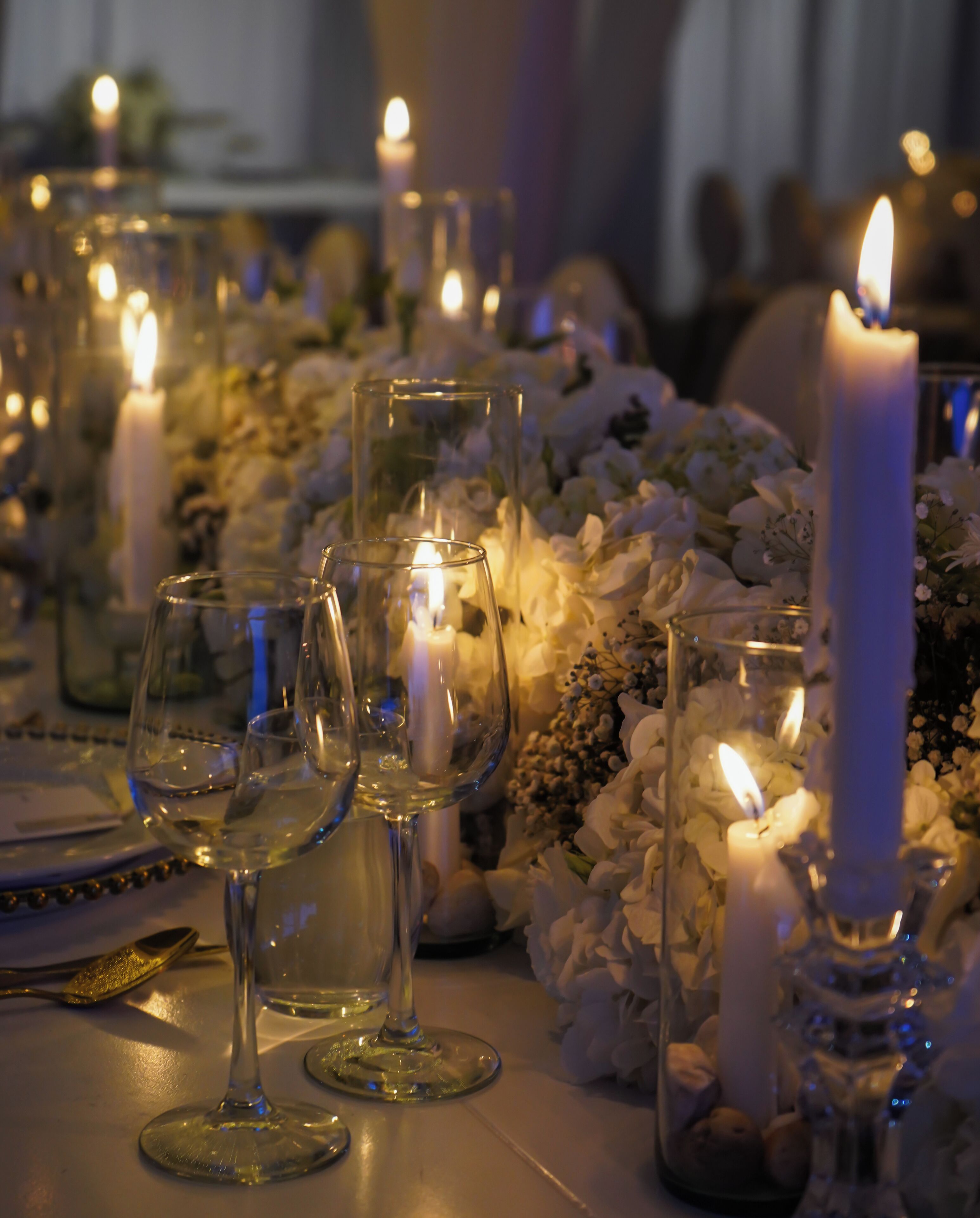 A table set with white wine glasses, candles, and floral arrangements.