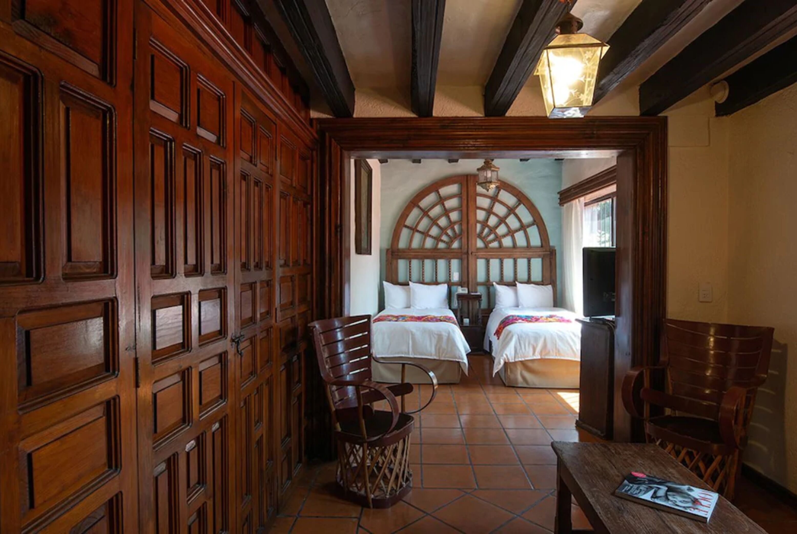 A hotel room with two beds, wooden furniture, and a tiled floor.