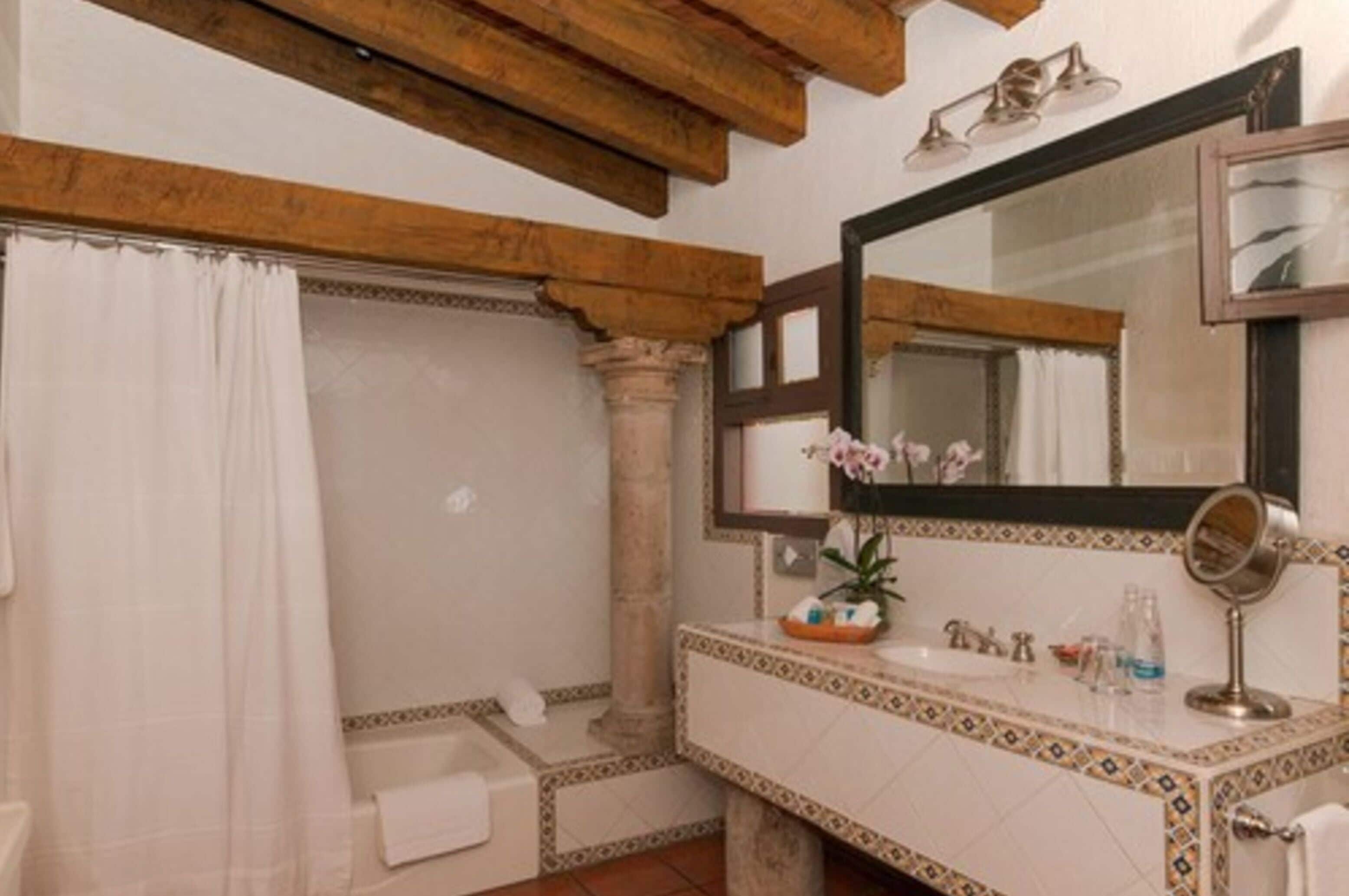 A bathroom with a wooden ceiling, a large mirror, a sink with a decorative tile border, and a shower curtain.