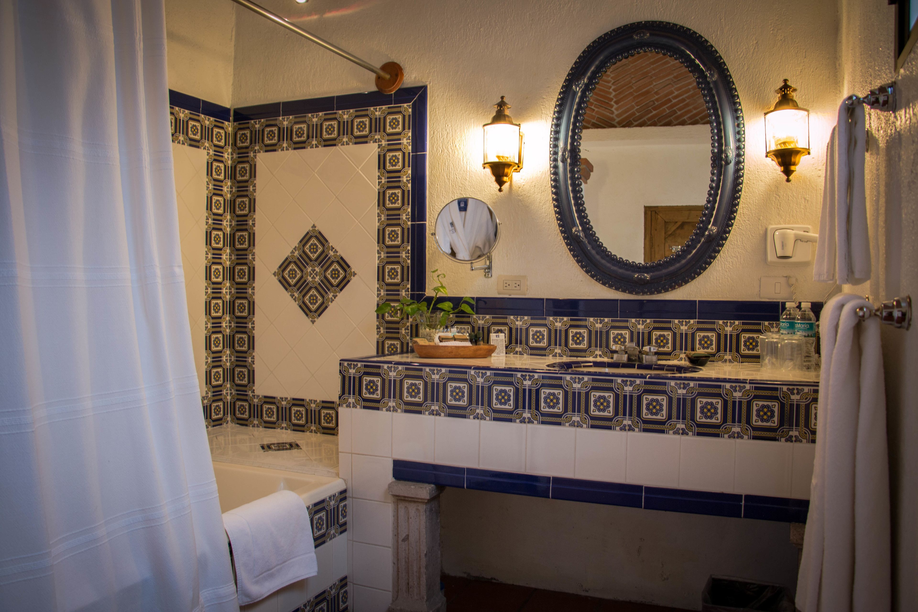 A bathroom with a patterned tile backsplash, a large mirror, and a sink with a towel hanging on the wall.
