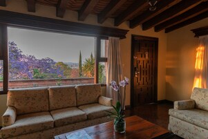 A living room with a sofa, a coffee table, and a view of a garden through a large window.