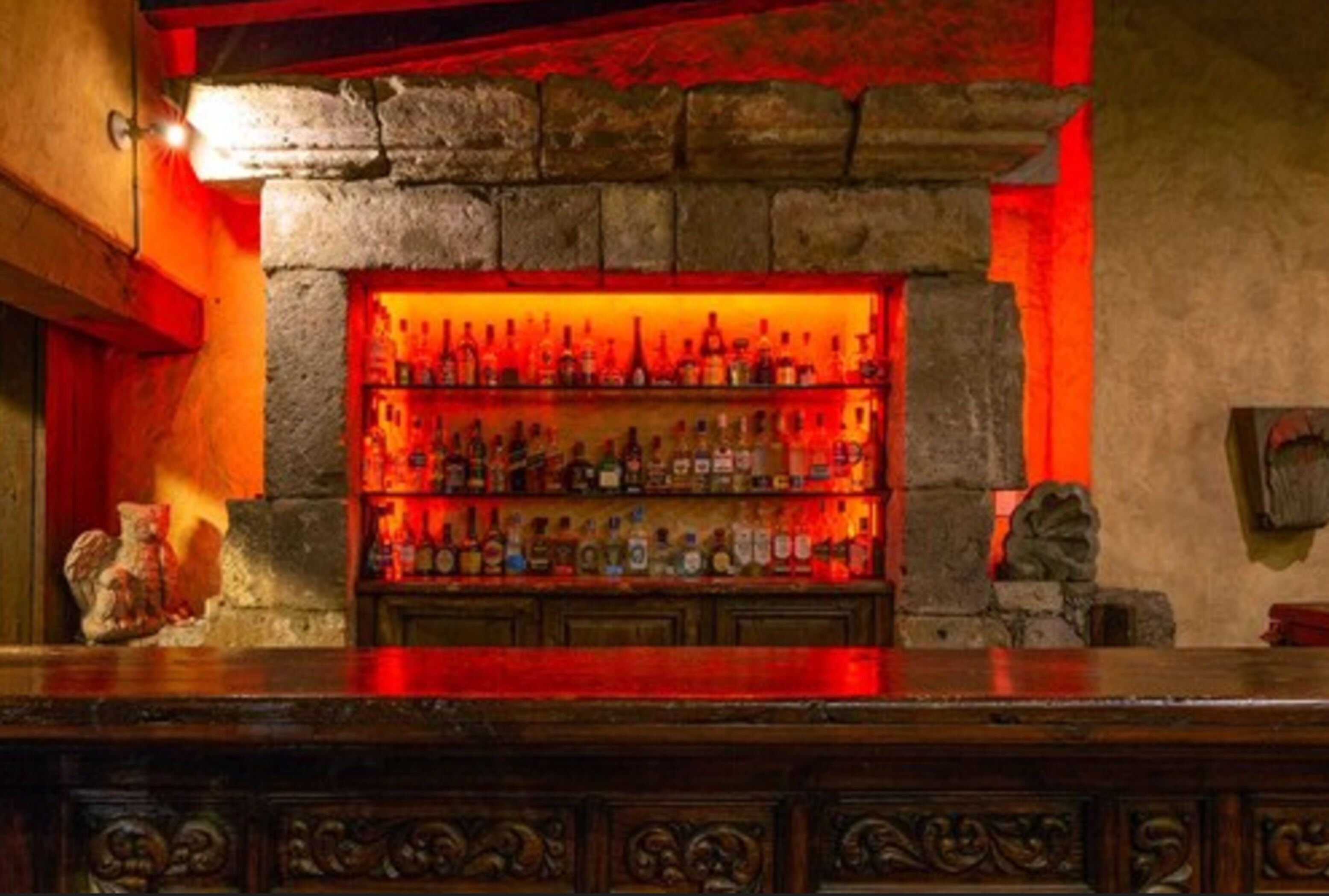 Uma área de bar com prateleiras cheias de garrafas e um fundo de parede de pedra.