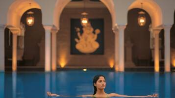 A person in a swimming pool with arched structures and a Buddha statue in the background.