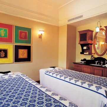 A hotel room with two beds, a vanity with a mirror, and framed artwork on the wall.