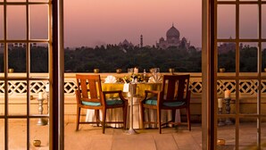 A dining table set for four with chairs, a view of a domed building in the background, and a balcony railing. - The Oberoi Amarvilas, Agra (Agra)