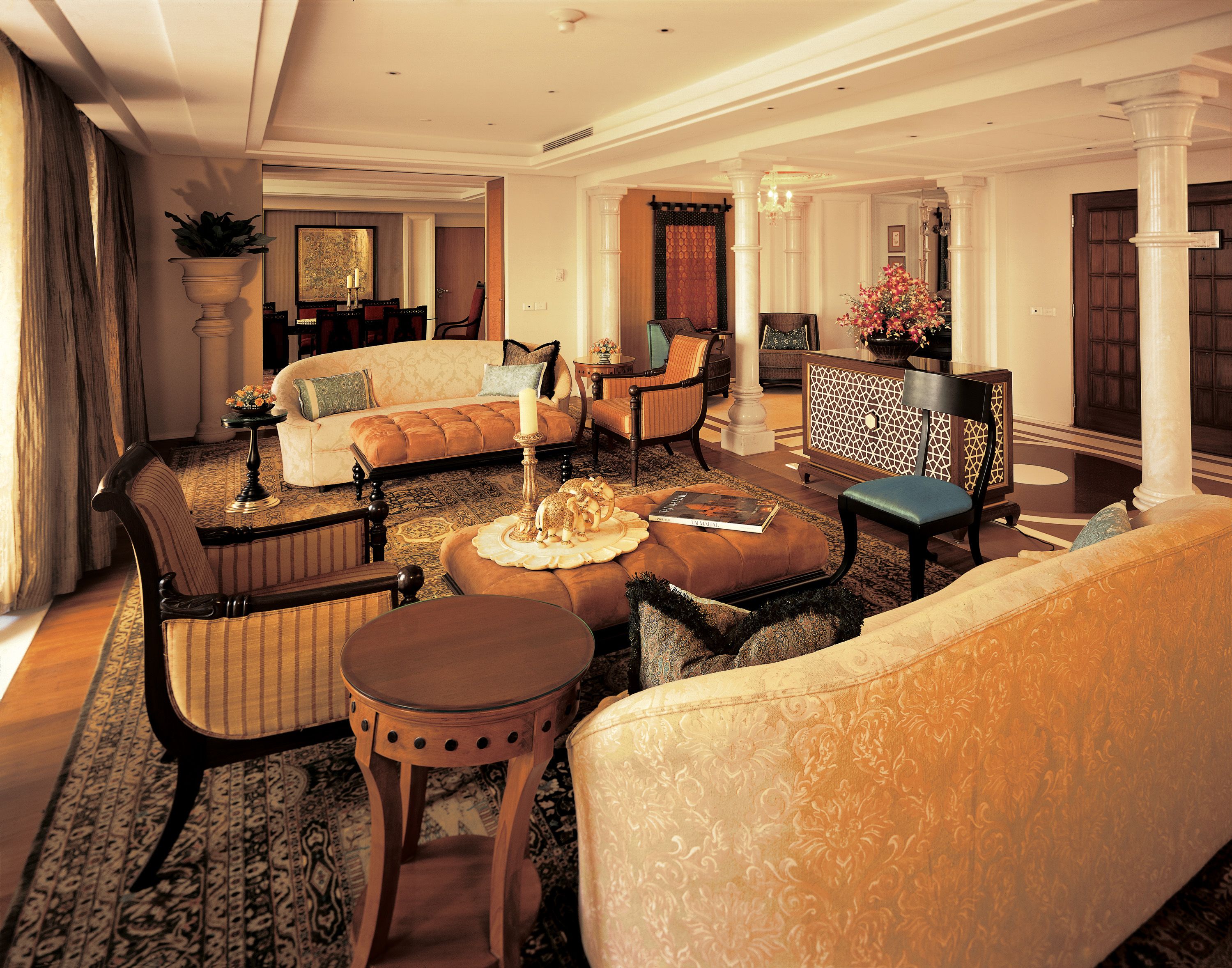 A spacious living room with a large sofa, a smaller armchair, and a coffee table. There is a decorative lamp and a potted plant on the coffee table.