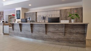 A modern reception desk with a wooden finish, a mounted computer, and a potted plant. - YORS Hotel Hannover (Hannover)