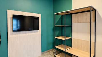 A room with teal walls, a white radiator, a black TV mounted on a wooden frame, and a black metal shelving unit with wooden shelves.