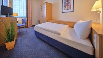 Ein Hotelzimmer mit Bett, Schreibtisch mit Computer, Stuhl, Kleiderschrank und einer Zimmerpflanze.