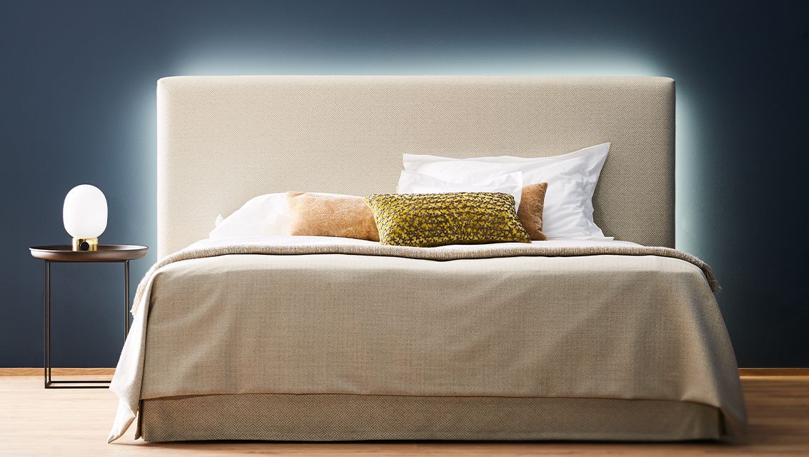 A bed with a headboard, a bedside table with a lamp, and a patterned pillow.