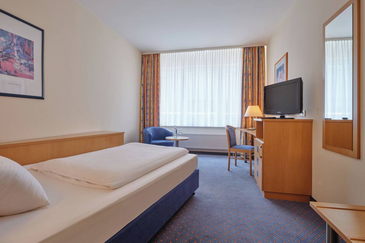 A hotel room with a bed, a desk, a chair, a television, and a window with curtains.