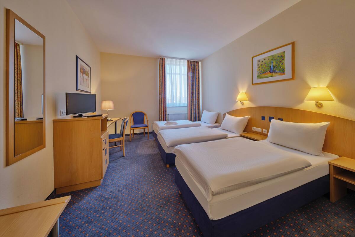 A hotel room with a desk, two beds, a chair, and a television.