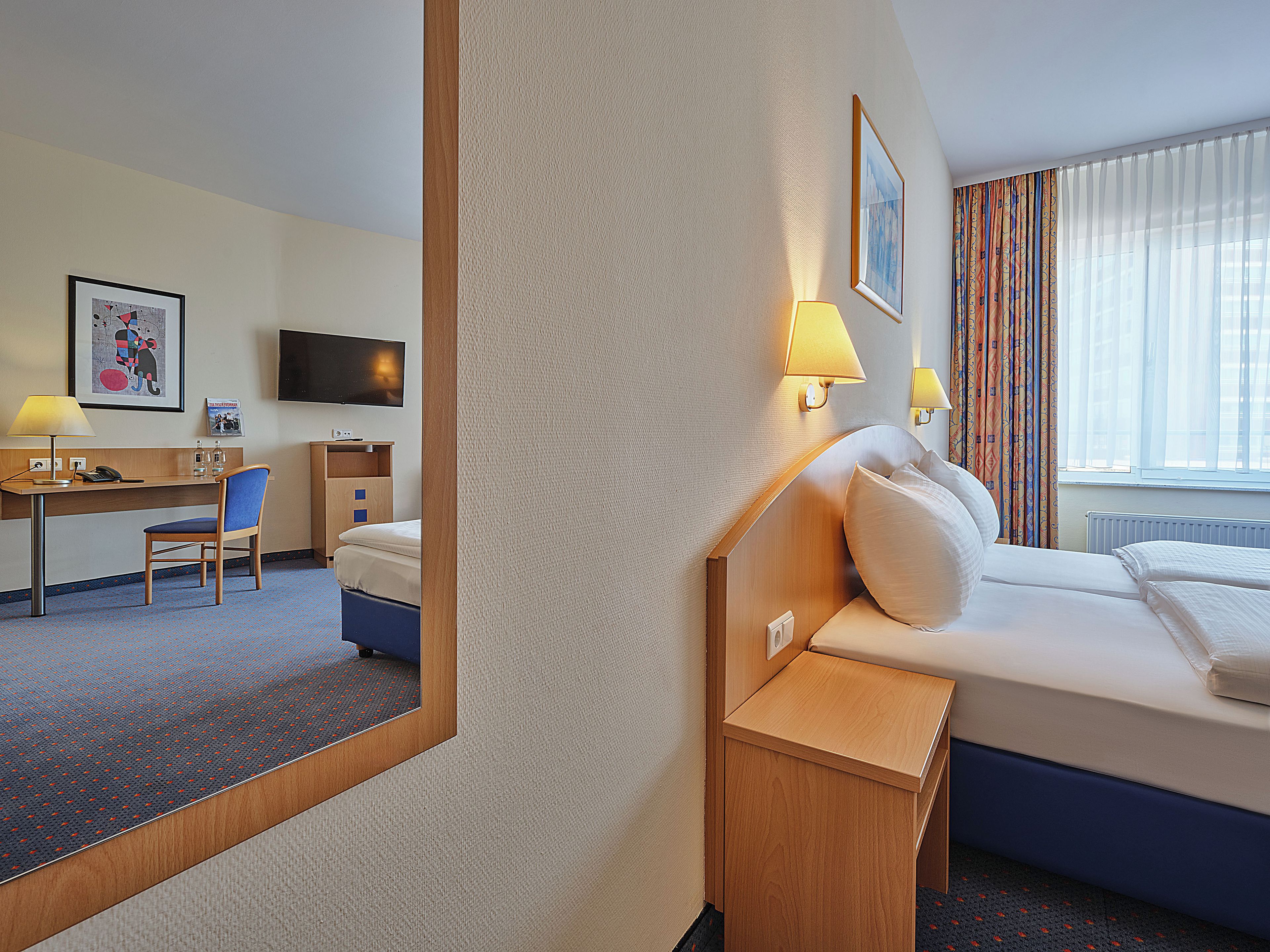 A hotel room with a bed, desk, chair, and a television on the wall.