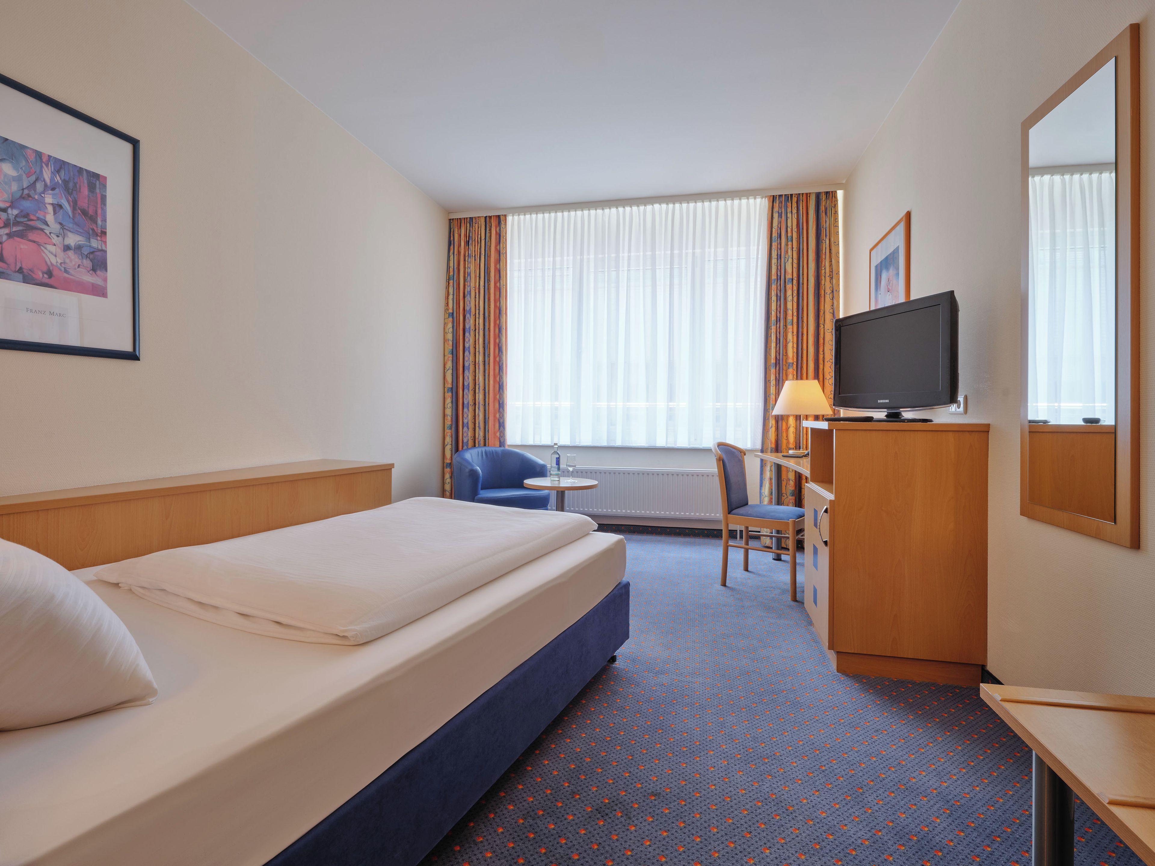 Une chambre d’hôtel équipée d’un lit, d’un bureau, d’une chaise, d’une télévision et d’une fenêtre avec des rideaux.