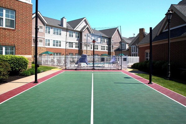 A tennis court with a white fence, surrounded by brick houses and a clear sky.