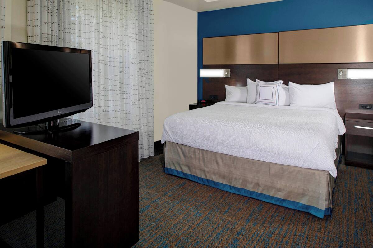 A hotel room with a bed, a TV on a desk, and a nightstand.