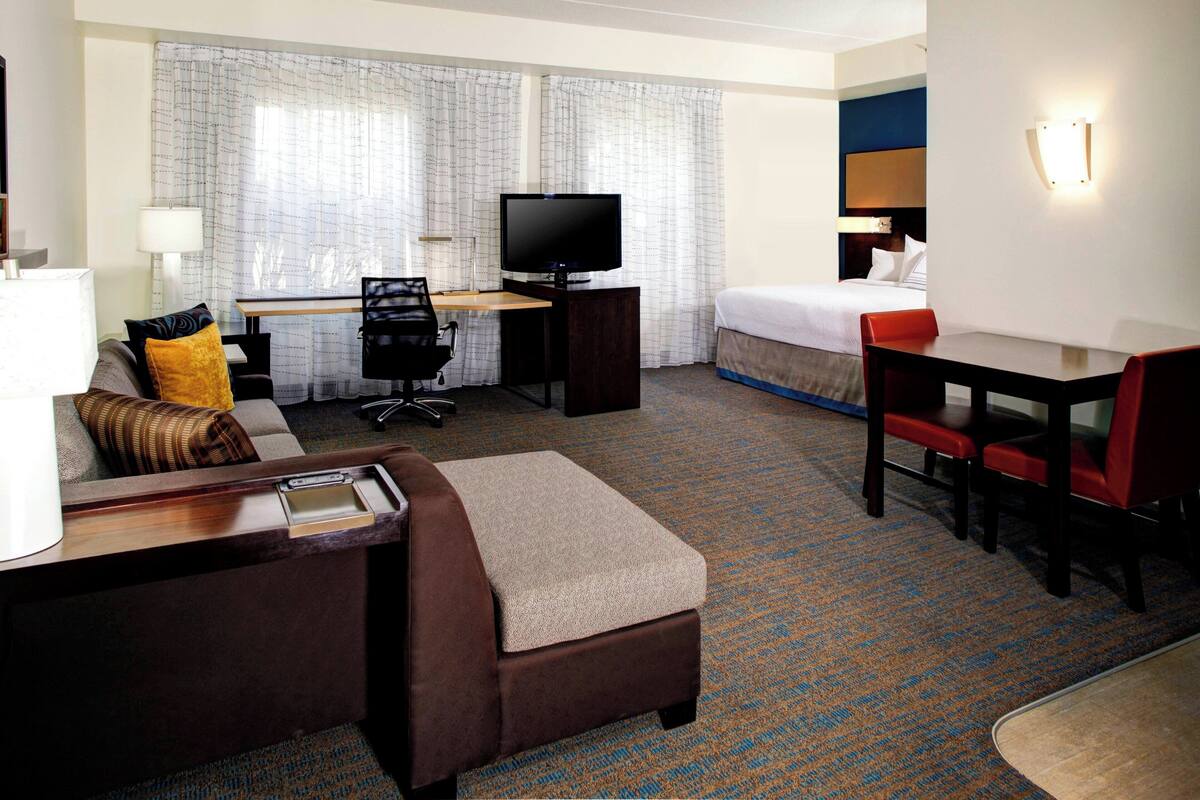 A hotel room with a bed, a desk with a television, a sofa, and a small table.