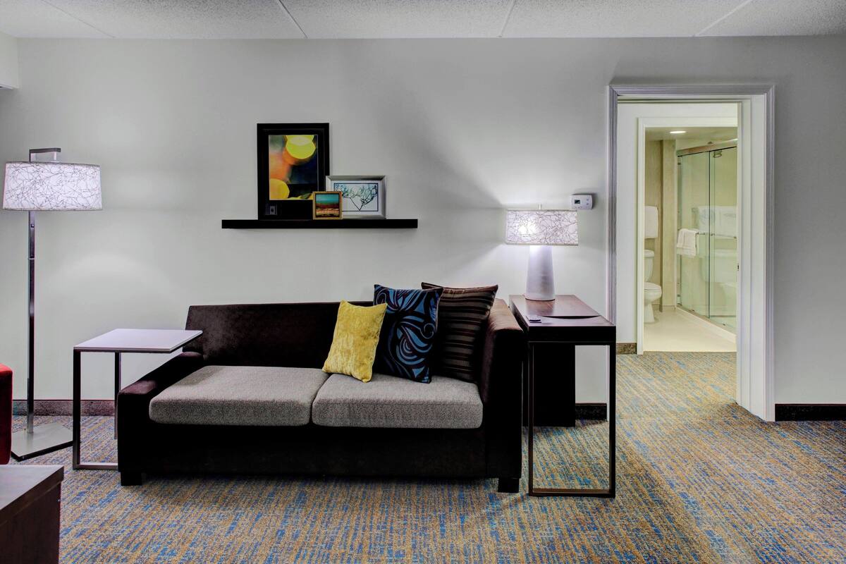 A hotel room with a sofa, two lamps, a small table, and a framed picture on the wall.