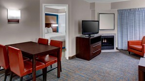 Une chambre d’hôtel avec une table à manger, des chaises rouges, un téléviseur à écran plat, une cheminée et une grande fenêtre avec des rideaux.