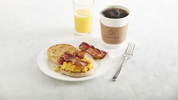 En morgenmadstallerken med æg, bacon, ristet brød, et glas appelsinjuice og en kaffekop.
