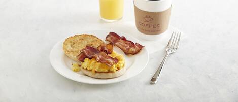 A breakfast plate with eggs, bacon, toast, a glass of orange juice, and a coffee cup.