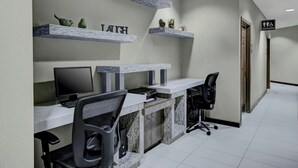 Un espace de bureau moderne comprenant un bureau, un ordinateur et des chaises de bureau. On y trouve des étagères décoratives avec des plantes et un panneau indiquant la direction des toilettes.