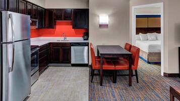 A compact hotel room with a kitchenette, a dining area with a table and chairs, and a bed with a headboard.