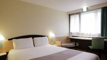A hotel room with a large bed, a desk with a chair, and a window with curtains.