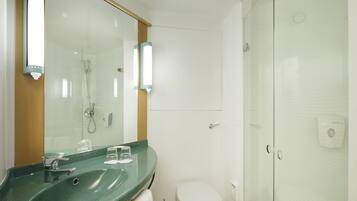 Un baño con un lavamanos verde, un espejo, un inodoro blanco y una cabina de ducha con paredes de vidrio.