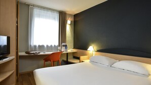Ein Hotelzimmer mit Bett, Schreibtisch, Stuhl, Fernseher und einem Fenster mit Vorhängen.