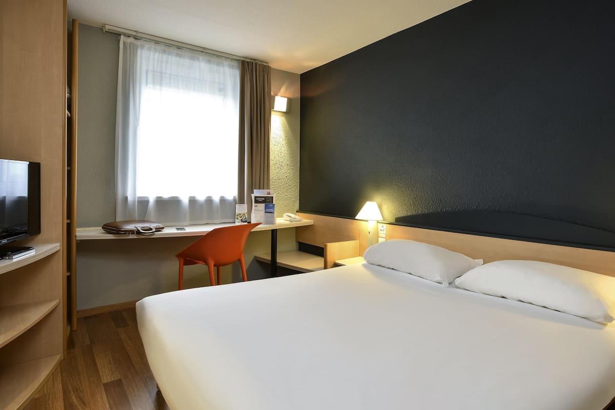 A hotel room with a bed, a desk, a chair, a television, and a window with curtains.
