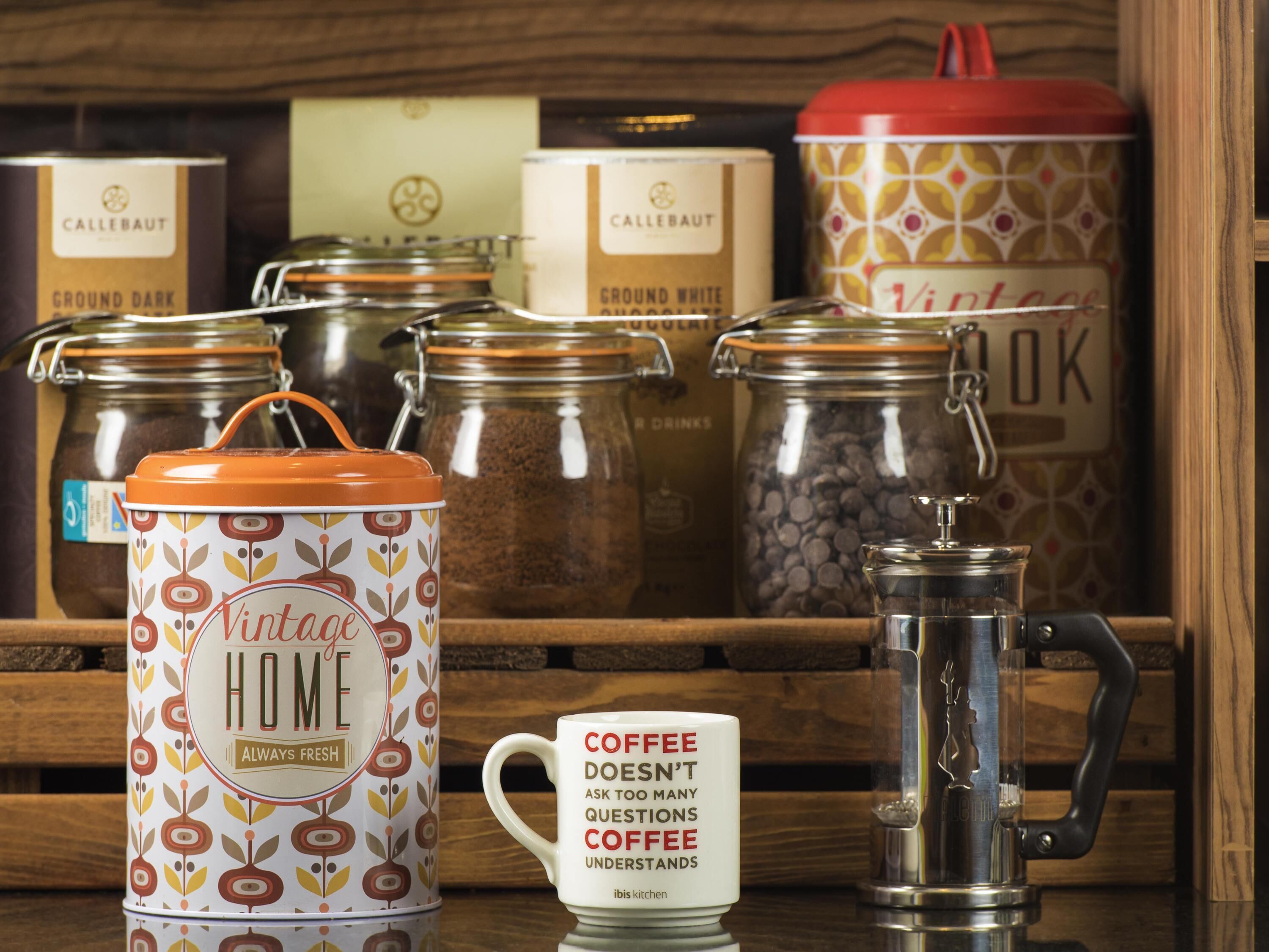 Una estación de café con un recipiente metálico de estilo vintage con la etiqueta 'Vintage Home' y una taza de café con un mensaje.