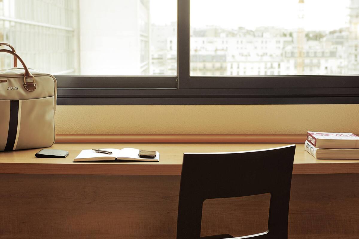 Een bureau met een handtas, een notitieboekje, een pen, een smartphone en een stoel.