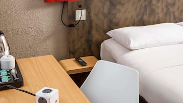 Habitación de hotel con un escritorio de madera, una regleta de enchufes blanca, un control remoto, una cama con ropa blanca y una pared de acento roja.