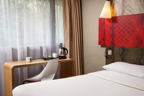 Una habitación de hotel con cama, escritorio, silla, cafetera y lámpara.
