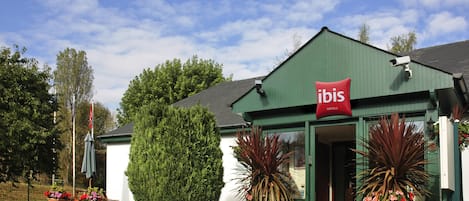 A green building with a red sign reading "ibis Hotels". There are potted plants in front of the building.