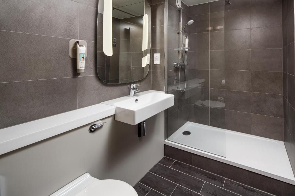 Un baño moderno con un lavamanos blanco, un espejo, cabina de ducha y un inodoro.