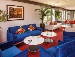 A modern lounge area with a blue sofa, two round tables, and a white couch. - ibis Coventry South (Coventry)