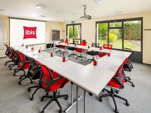 A conference room with a long table, red and black chairs, a projector screen, and a view of greenery outside. - ibis Coventry South (Coventry)