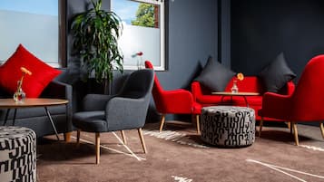 A modern lounge area with red and grey furniture, a large window, and a potted plant.