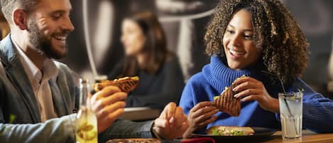 Una pareja cenando en un restaurante con ambiente informal, que cuenta con una mesa de madera, una bebida y un sándwich.