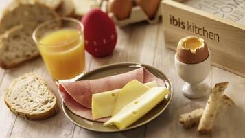 Una colazione con pane, uova, formaggio, prosciutto e un bicchiere di succo d'arancia su un tavolo di legno.